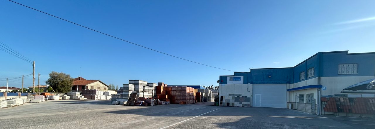 Armazém à direita, paletes de materiais a meia distância e linhas elétricas sobre o parque